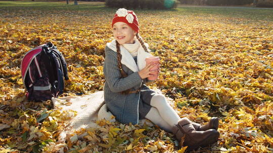 女孩拿着杯子坐在满是落叶的地上