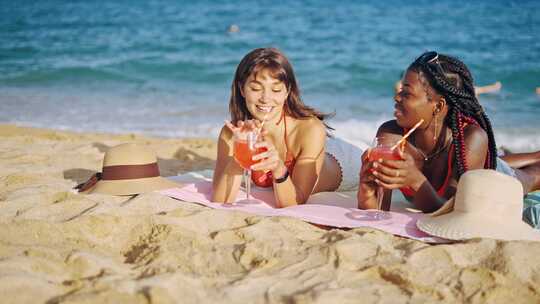 两个女孩躺在沙滩上喝饮料