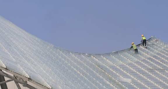 建筑工人城市高空安装作业 玻璃顶蓝天背景