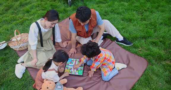 一家四口坐在野餐垫开心玩游戏