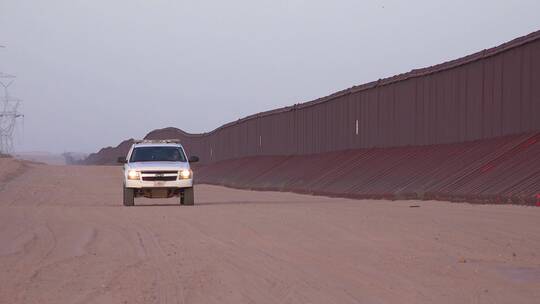 在边境墙旁边道路上行驶的边境巡逻车
