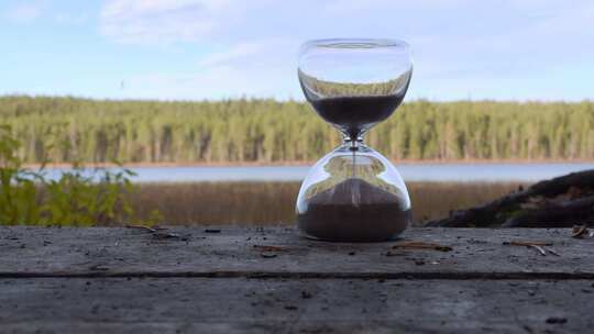小时玻璃沙子落下。时间就是金钱。肮脏的木质表面和芬兰自然上的时间玻璃