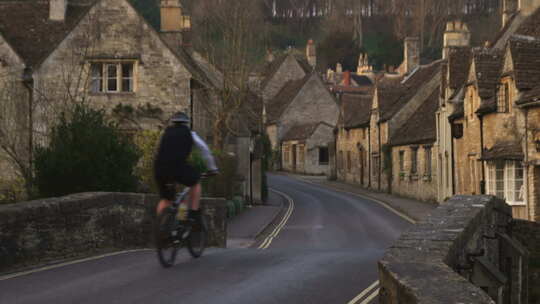 骑自行车的人穿过英国一个古老的石头村庄。