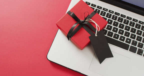 笔记本电脑和带黑色丝带和礼品标签的红色礼品盒，红色背景，带复制空间