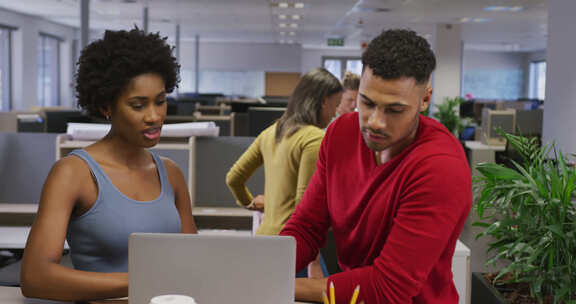 不同的男性和女性商业同事在办公室交谈和使用笔记本电脑