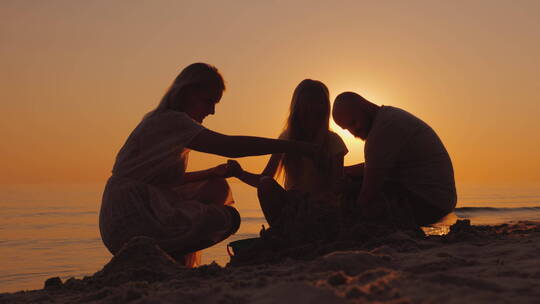 黄昏时分一家人在海滩堆城堡的剪影