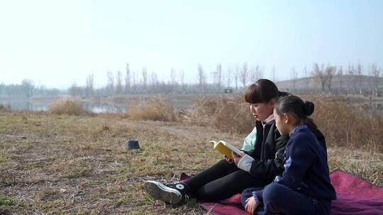 冬季在公园草坪上看书的母亲和两个女儿