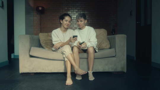 两个女人拿着手机坐在家里的沙发上
