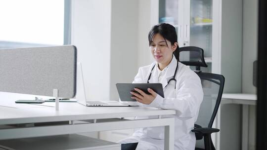 年轻女医生在办公室使用笔记本和平板工作视频素材模板下载