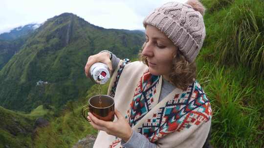 穿着雨披的旅行者女人在山里露营时喝茶