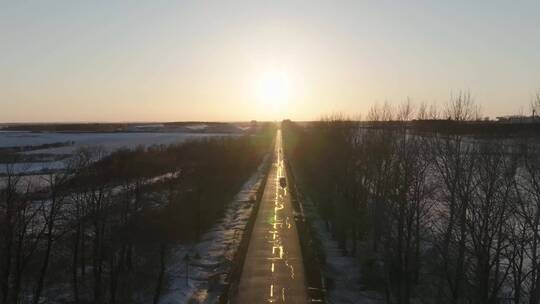 雪地公路迎着夕阳孤独行驶航拍