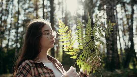 一位被大自然拥抱的年轻女子手持蕨类植物，