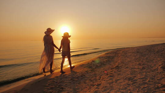 母亲和女儿在日落的海边散步