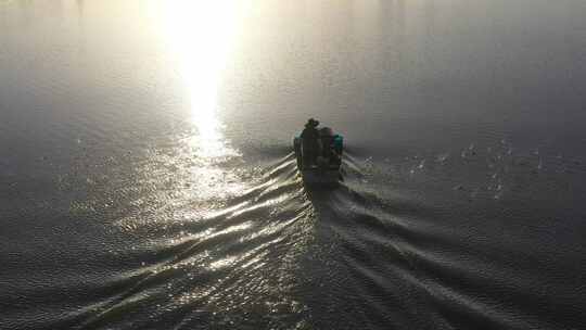 夕阳中两农民乘船在鱼塘抛撒饲料