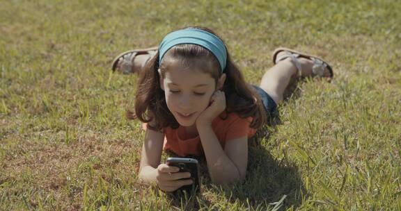 女孩趴在草坪上玩手机