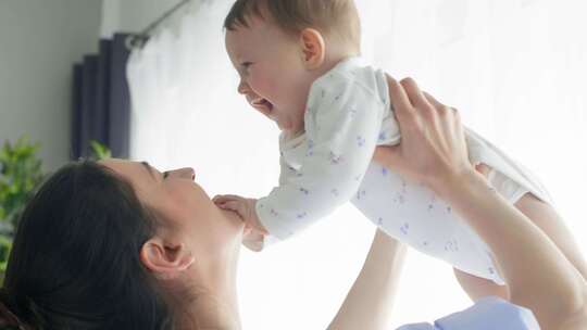 女人把婴儿举到空中，亲吻她的脸颊