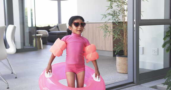 戴太阳镜和粉色游泳圈的出生女孩为泳池时光