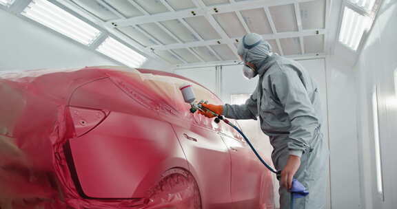 一个穿着防护服和口罩的汽车画家正在喷漆
