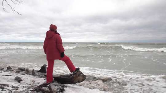 身着温暖红色衣服的女孩站在北方暴风雨大海的岸边