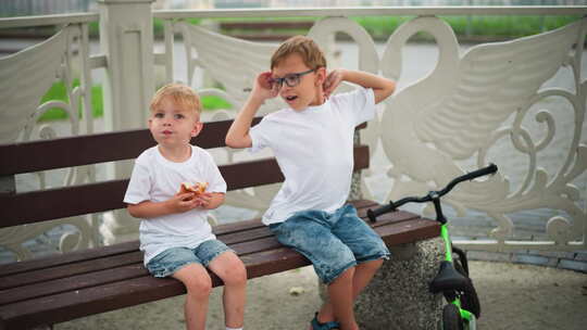 两个兄弟姐妹坐在一起，年幼的孩子拿着零食