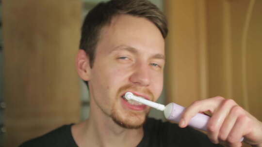 一个红胡子的年轻人正在用白色电动刷子刷牙