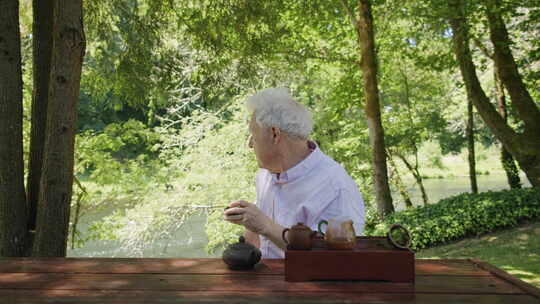 老人从水罐里倒茶，啜着茶，看着河边，茶壶
