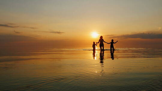 日落时分母亲带着两个孩子走在浅水区玩耍
