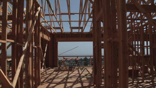 一个男人光着膀子拿着一根木头走进一座正在建设的房子里