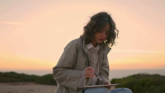 宁静的女人在傍晚的海崖画画