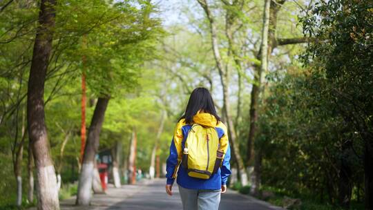 春天年轻女孩背着包在公园路上边走边看美景