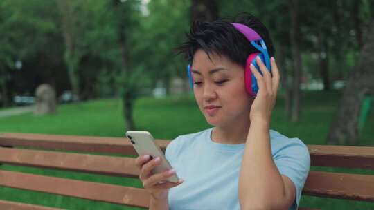 戴耳机在公园长椅上欣赏音乐的女人