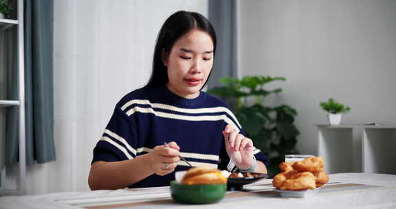 年轻的亚洲女人在家里的餐桌上享受美食。