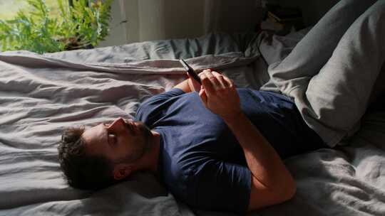 无聊的男人躺在床上浏览手机