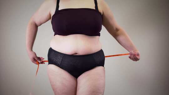 无法辨认的肥胖高加索女人测量臀部。穿着内