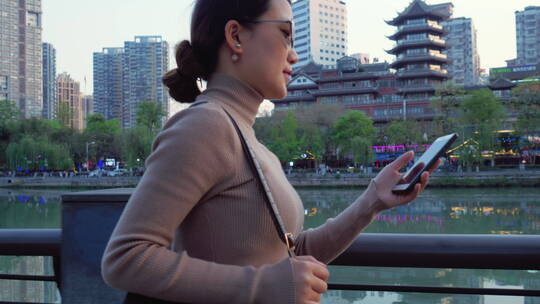 商务美女拿着手机走在成都锦江九眼桥河边