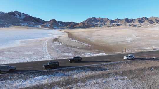 航拍冬季新疆赛里木湖雪山环湖公路夕阳车辆