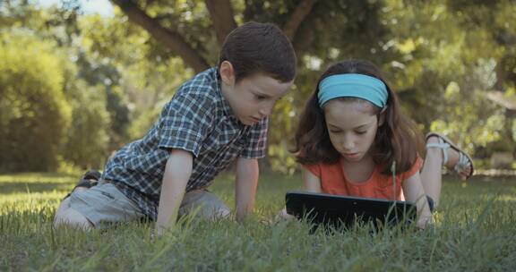 小孩在草地上玩平板电脑