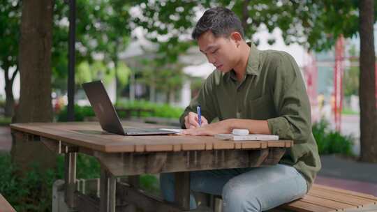 学习并做笔记。亚洲男子正在网上学习，一边