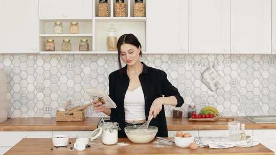 女人在搅拌碗里搅拌面粉时看着食谱