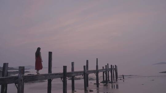 海边独走在木桥上的穿红裙子的女孩走向大海