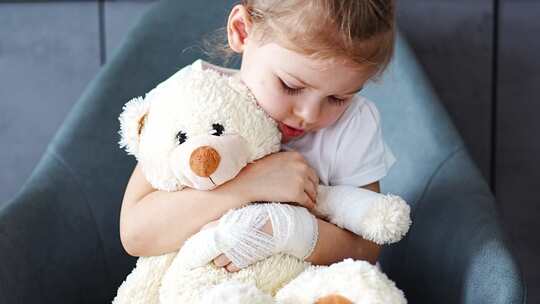 指头受伤的小女孩用绷带缠住的手抱着泰迪熊