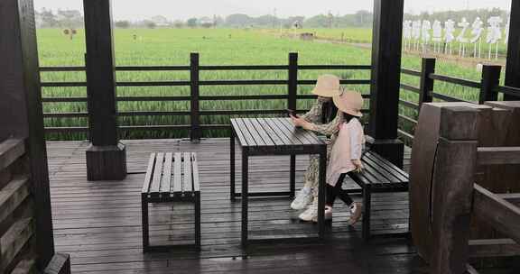 妈妈与女儿在稻田木亭中休息看手机