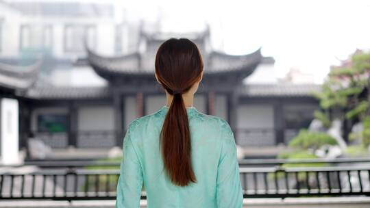 年轻旗袍女子走到中式合院连廊护栏边观景