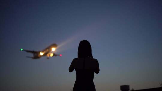 黄昏美女模特用手机拍摄飞机降落
