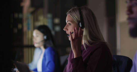 微笑的高加索女商人和同事晚上在办公室工作时使用耳机的视频