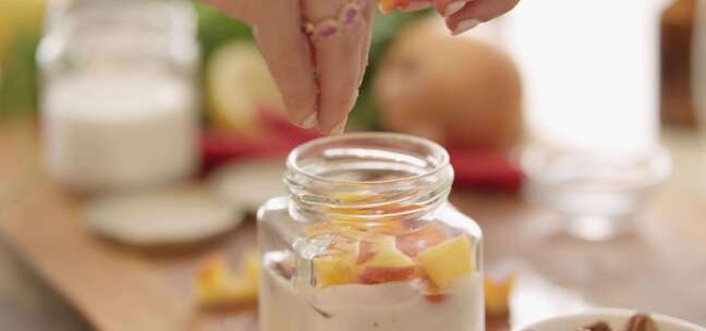 女人在厨房的小玻璃罐里给酸奶添加水果和坚