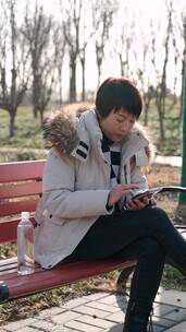 坐在公园长椅上使用手机的东方女性