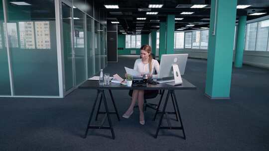 加班年轻女商人坐在办公室的办公桌前，在电脑上工作