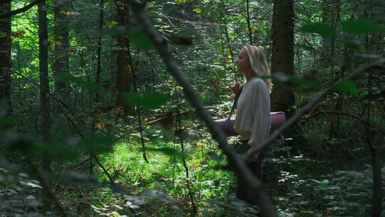 女人拿着瑜伽垫在树林里行走
