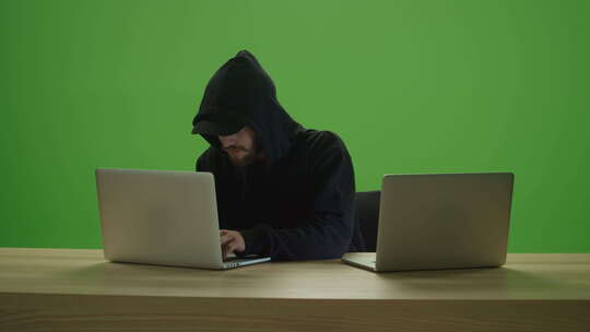 无法辨认的男子黑客穿着运动衫兜帽，在2台笔记本电脑上打字